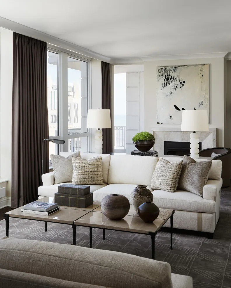 A pale beige sofa sits beside dark curtains and a slim-framed table in a bright room