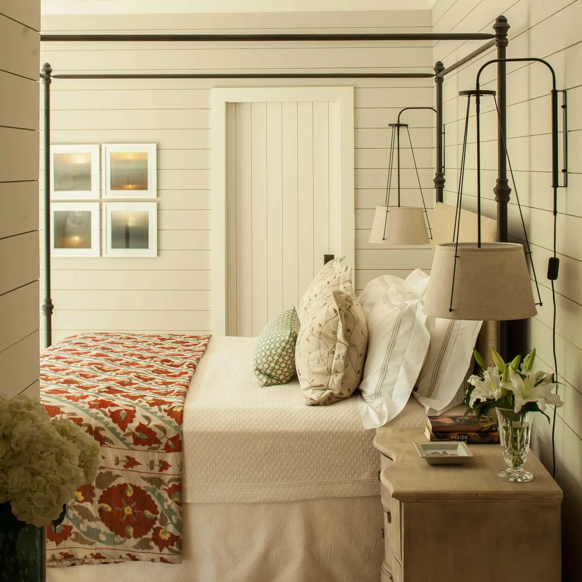 Dark wall brackets carry pale hanging shades beside a black four-poster bed against white horizontal boards.