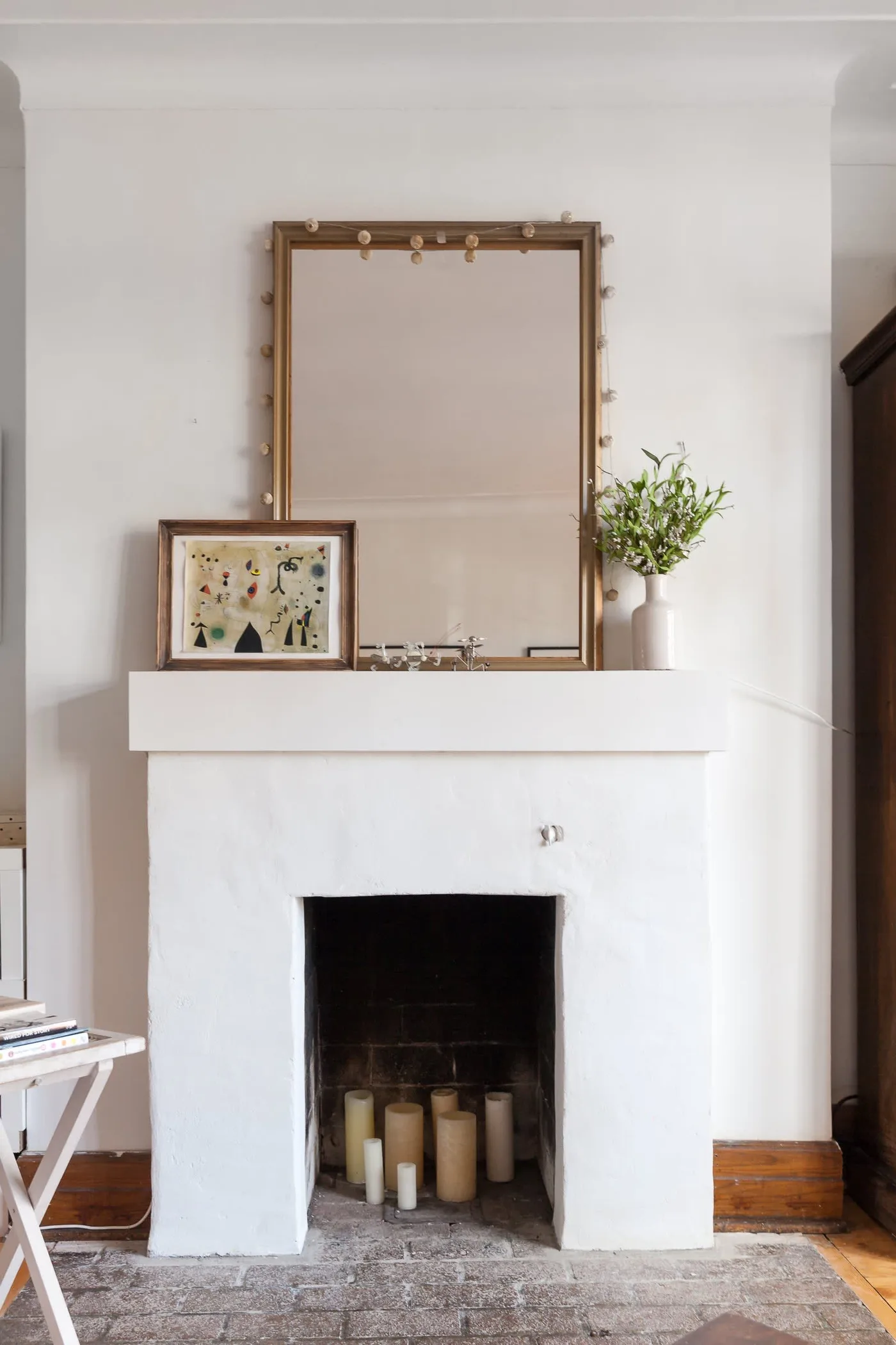 White fireplace with pale and cream pillars inside the dark opening, mirror and small picture on the mantel.