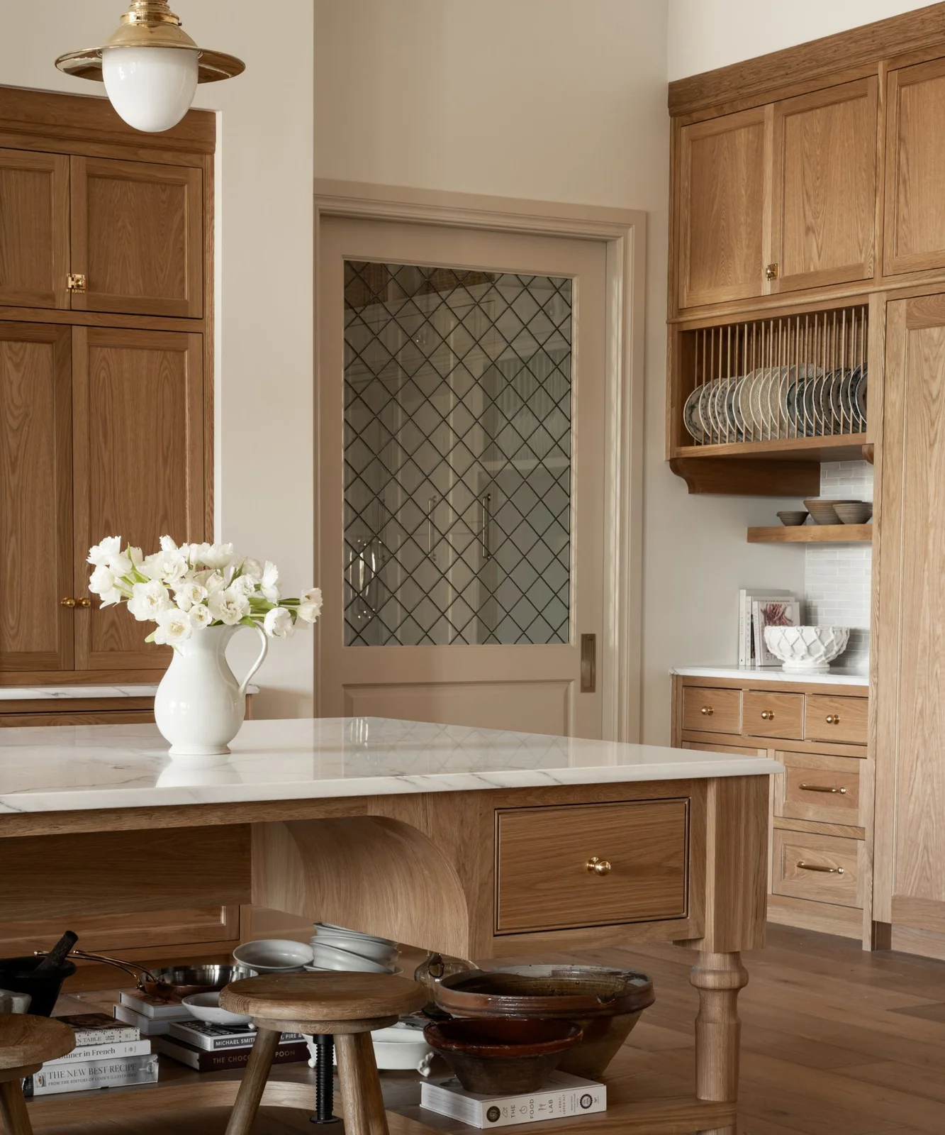 An open plate rack sits within white oak wall cabinetry above drawers near a glazed pantry door and a furniture-style island.