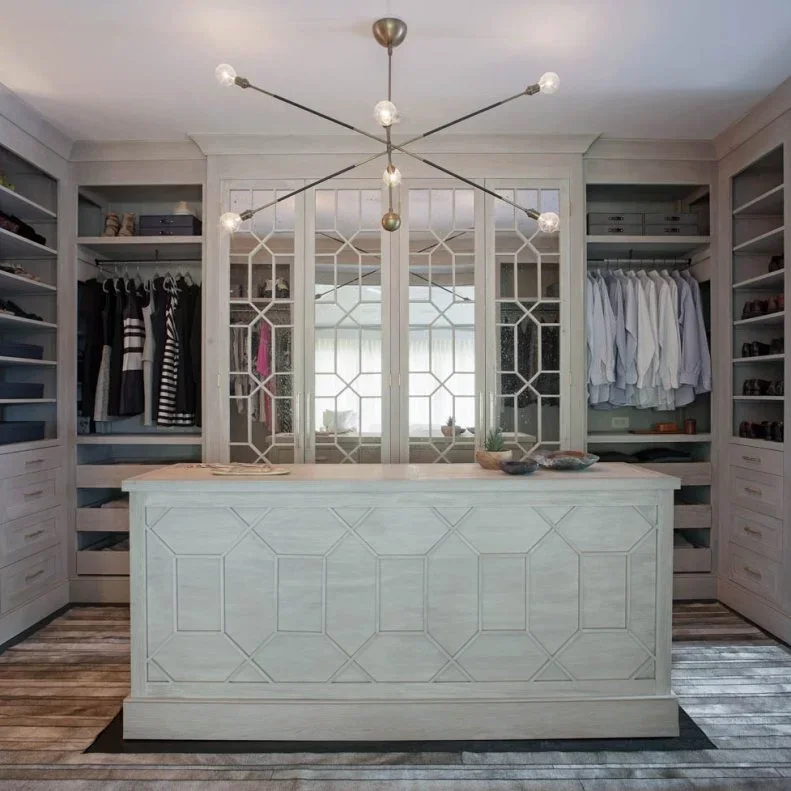 A pale gray closet has geometric mirrored doors behind a paneled island, with open hanging storage to either side.