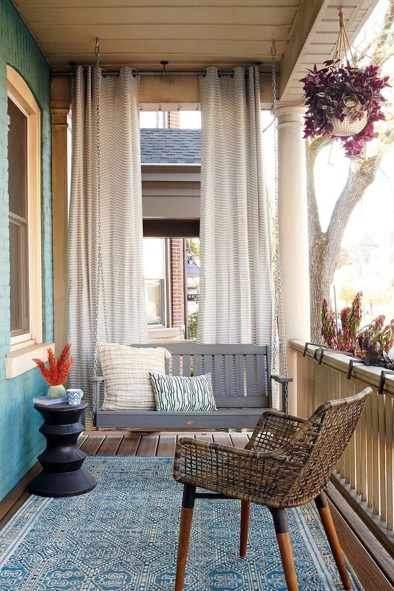 Turquoise porch with gray suspended swing, striped curtains, woven chair and blue patterned rug