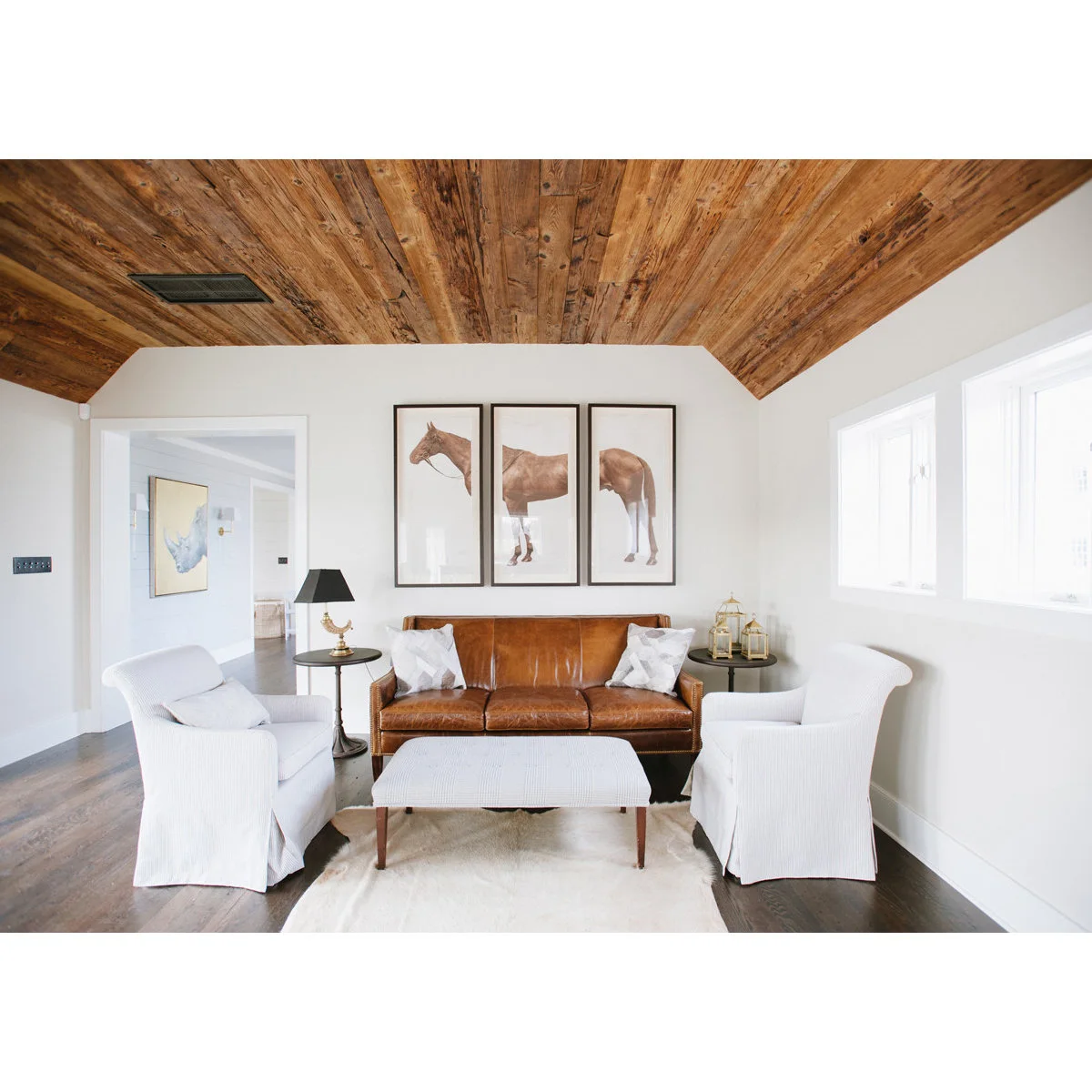 Compact white-walled living room with white chairs, a brown sofa and a wood ceiling