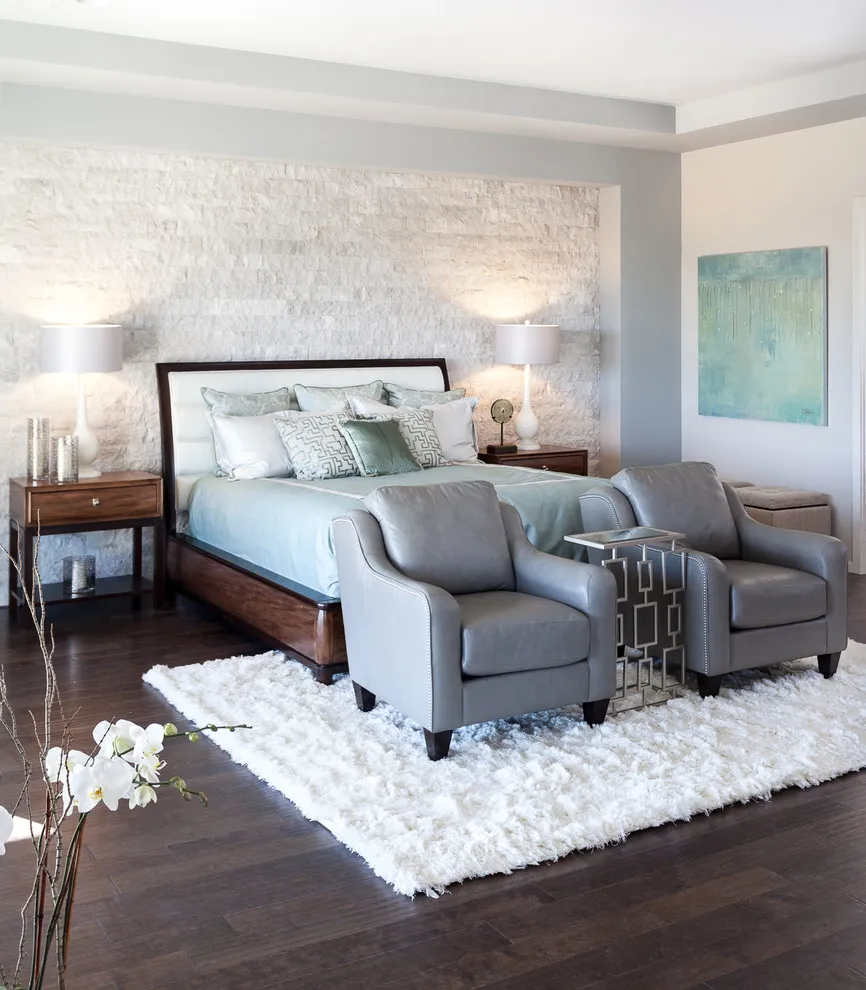 A light textured wall sits behind a timber bed beside soft gray chairs