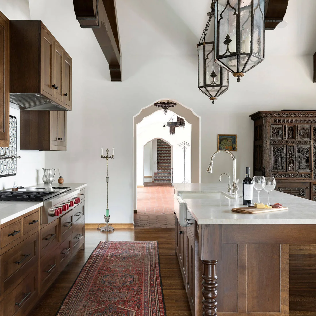 Two decorative lantern pendants hang over a timber kitchen island beside dark cabinets and shaped doorways.