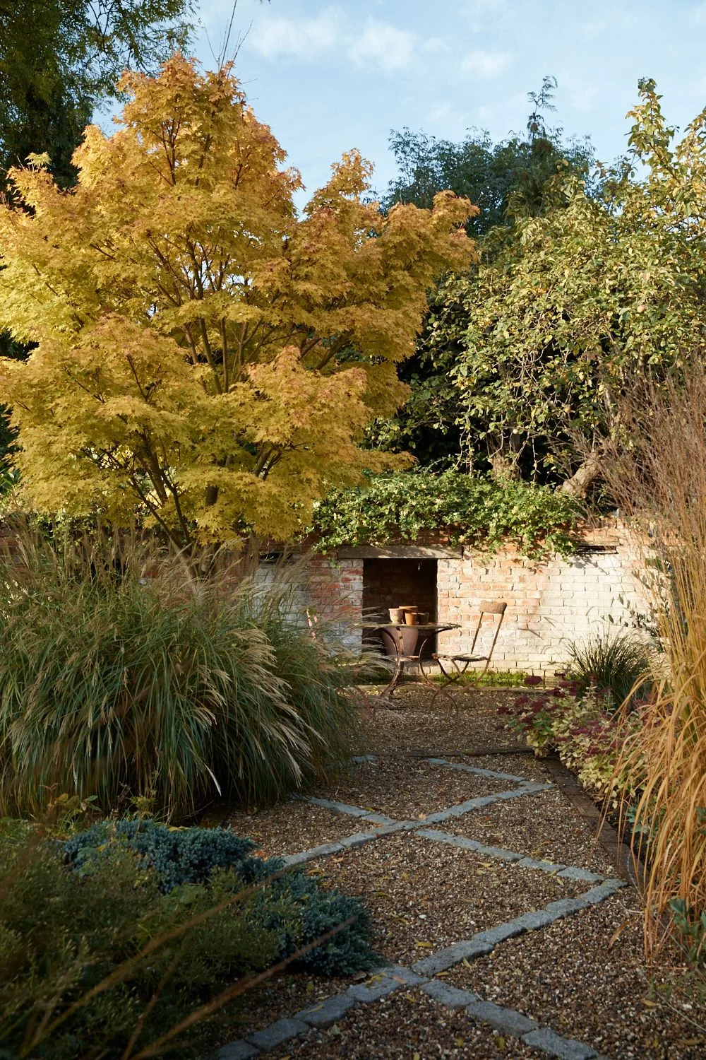 Stone strips form a diamond pattern across gravel beside a small garden table