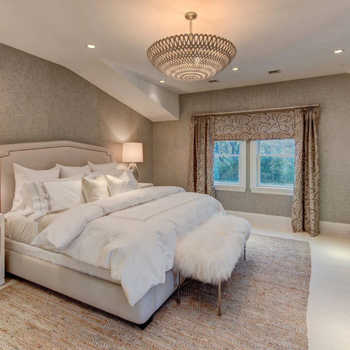 White shaggy upholstered bench on slim legs in a neutral bedroom with patterned curtains
