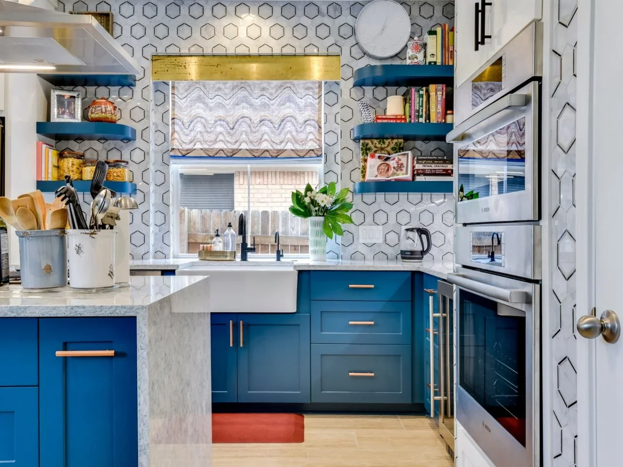 White patterned kitchen wall tiles with dark hexagonal outlines wrap around a window beside blue cupboards and shelves.