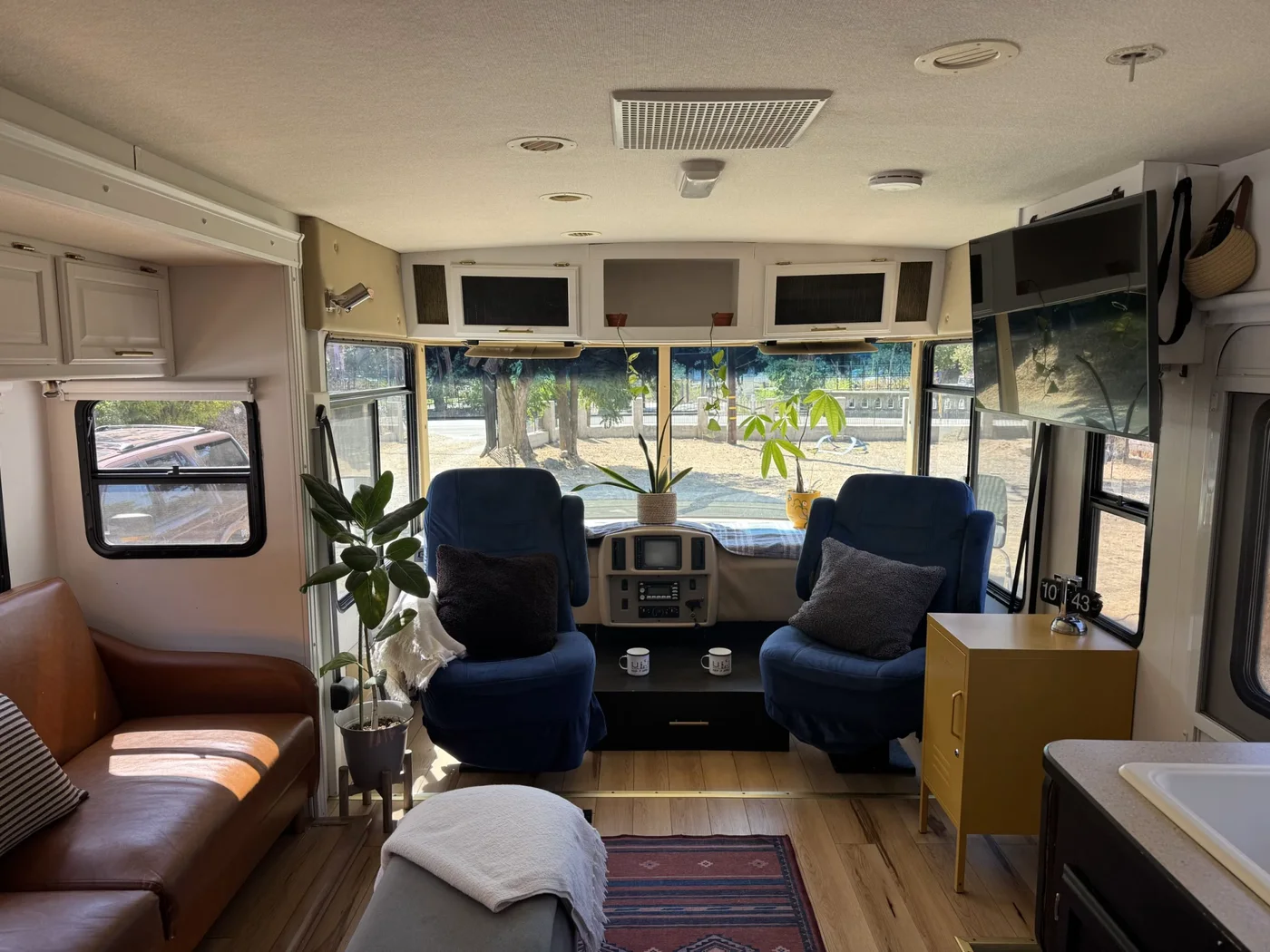 Motorhome front interior with two blue chairs, a brown sofa, small black table and mustard-colored cabinet.