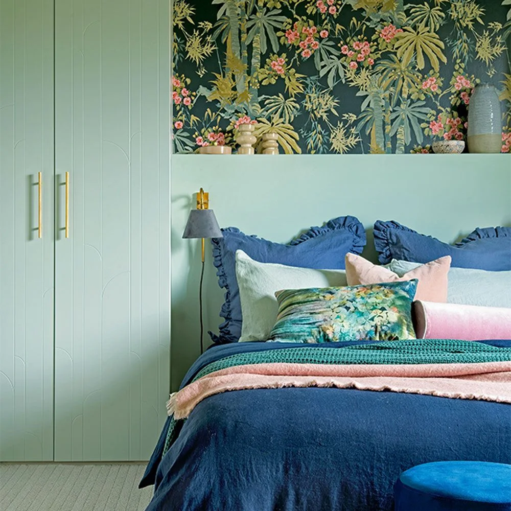 Pale green wardrobe with decorative vertical grooves beside a matching headboard and botanical wallcovering