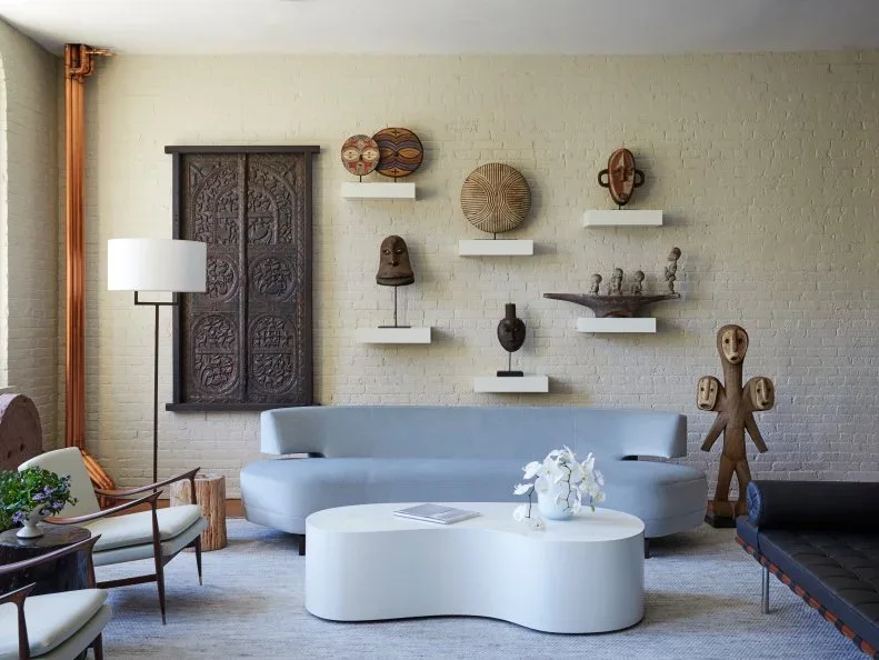 A pale blue sofa beneath floating shelves on white brick beside exposed vertical pipes