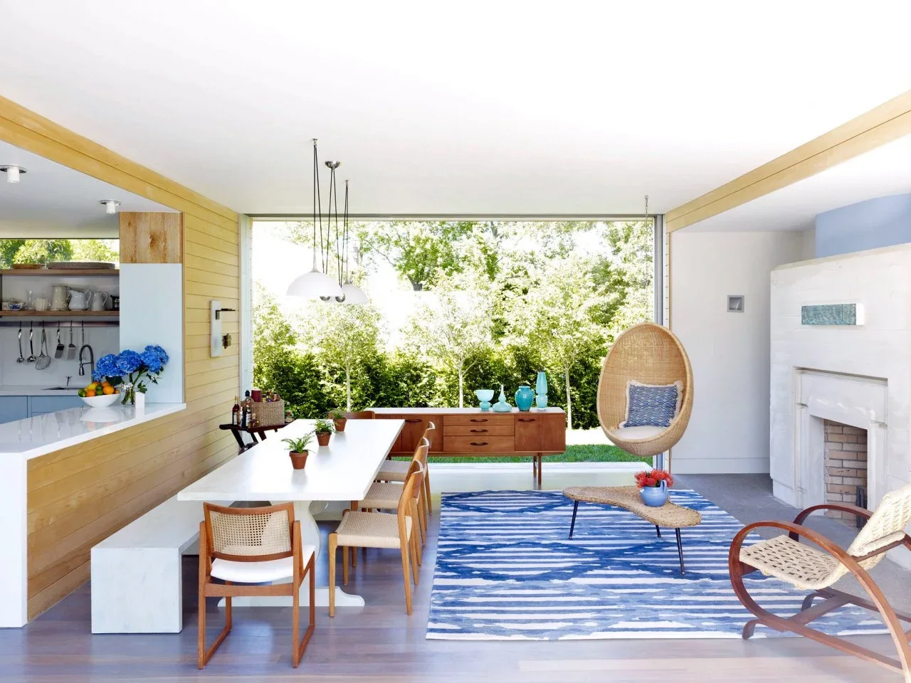 A low timber-clad divider separates a pale kitchen from an open dining and sitting area beside broad glazing.
