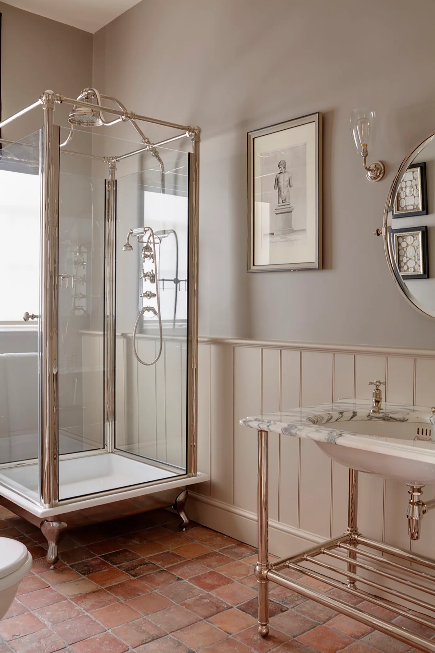 Traditional-style glass shower enclosure on shaped feet beside a console basin and pale paneled walls.