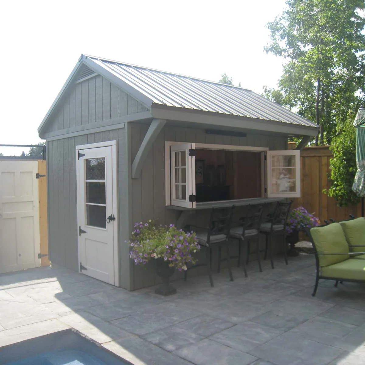 Grey garden bar shed with a glazed entrance door and open serving window above three stools