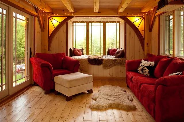 Deep red sofas sit beneath warm timber beams around a pale ottoman.