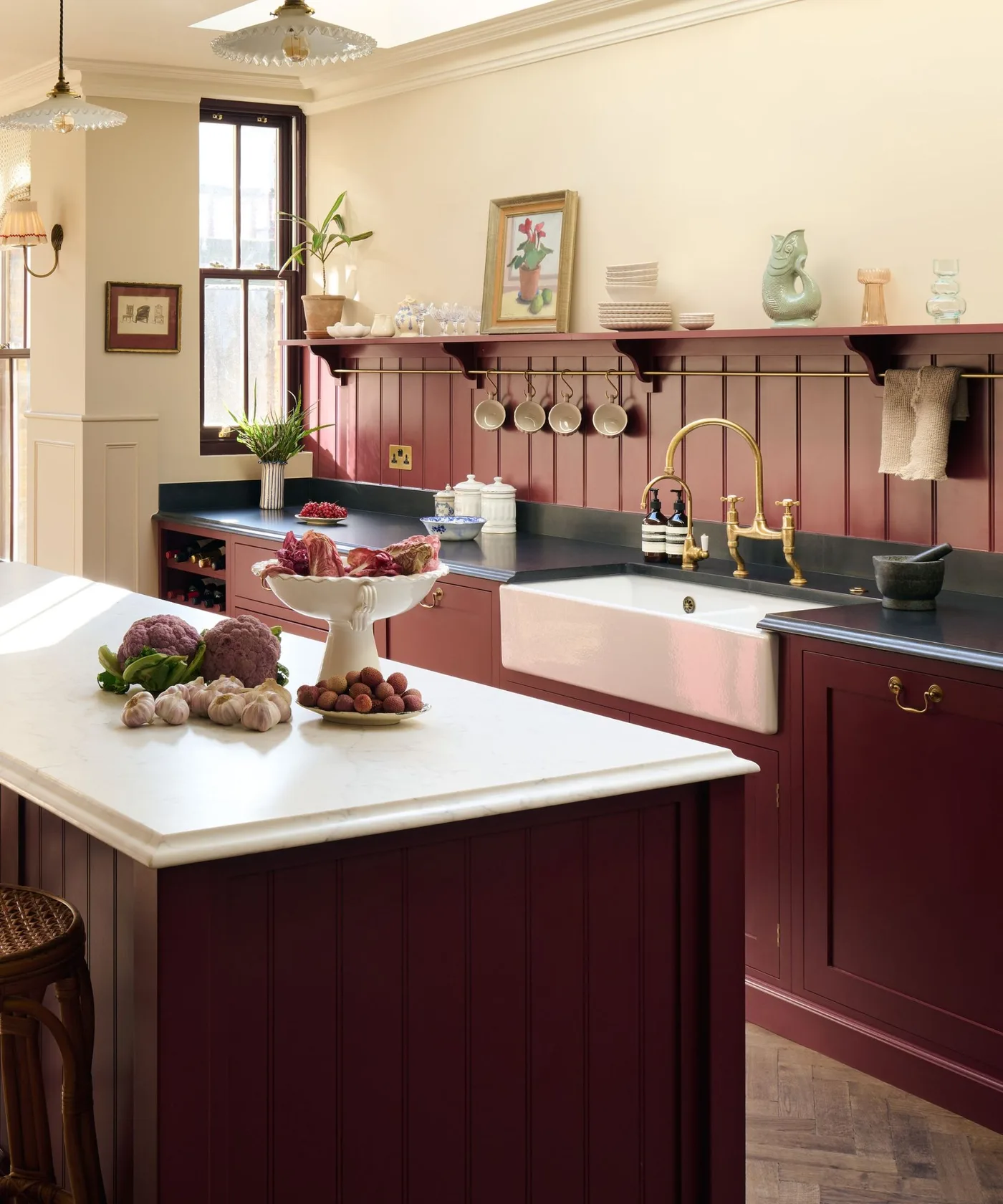 Burgundy kitchen cabinets and vertical paneling behind a white double sink, with a matching long shelf and black countertop.