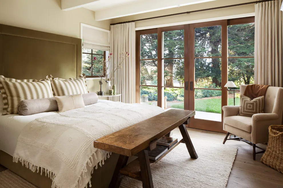 A pale beige bed faces a simple wooden bench beside tall garden doors