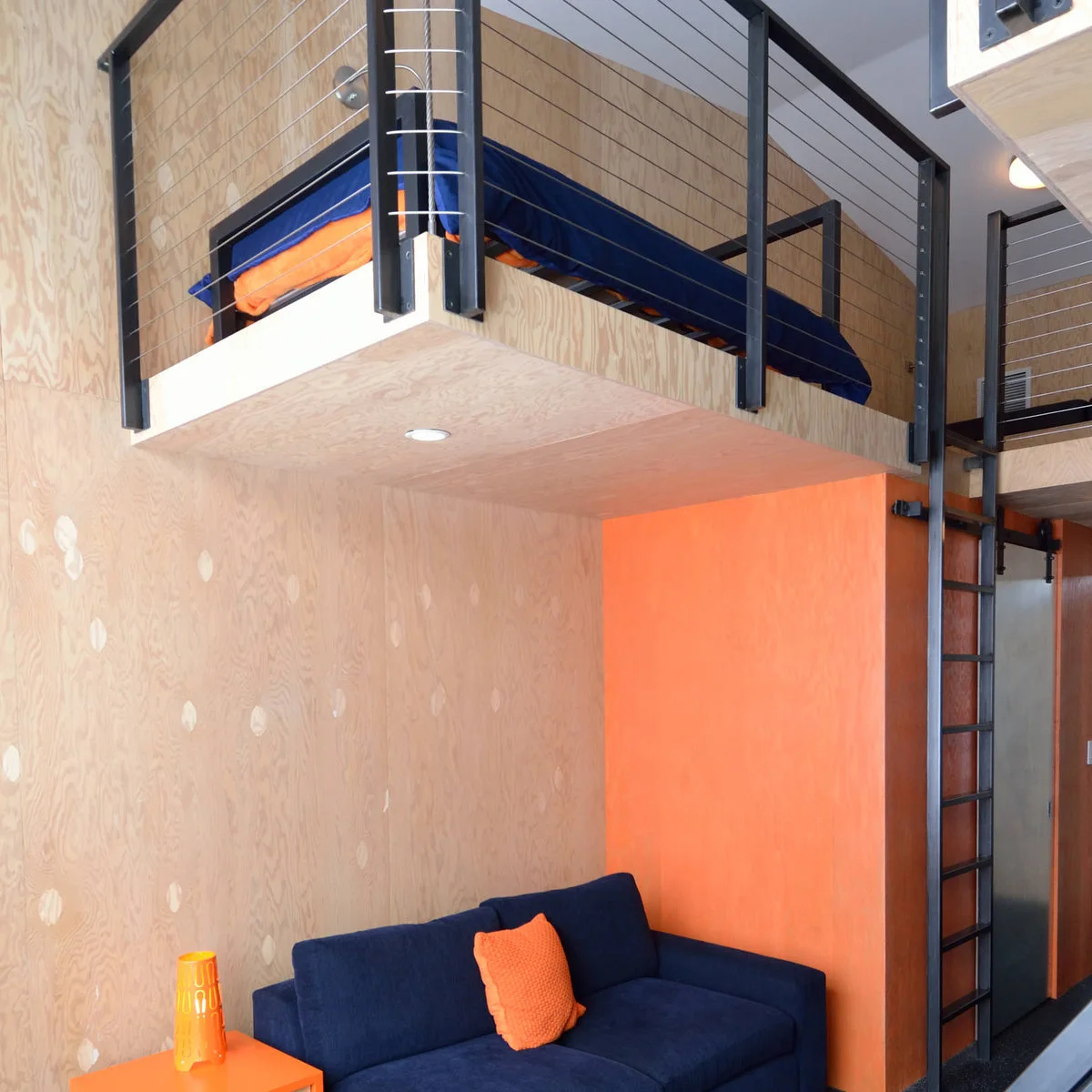 Plywood loft with dark posts and cable infill above a navy sofa against an orange wall.