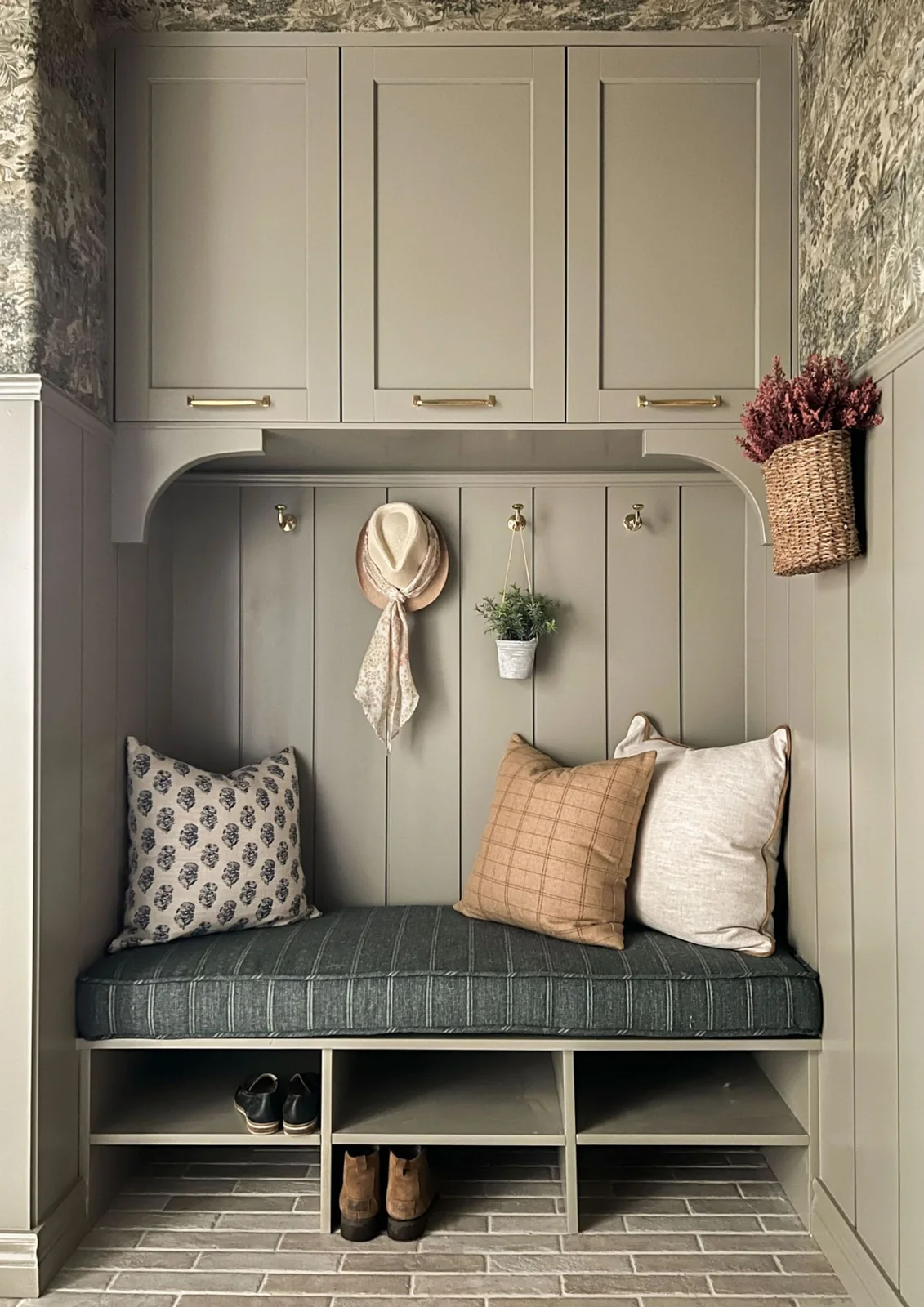 Muted green upper cabinets above a paneled hook wall and dark striped cushion with open shoe compartments near the floor.