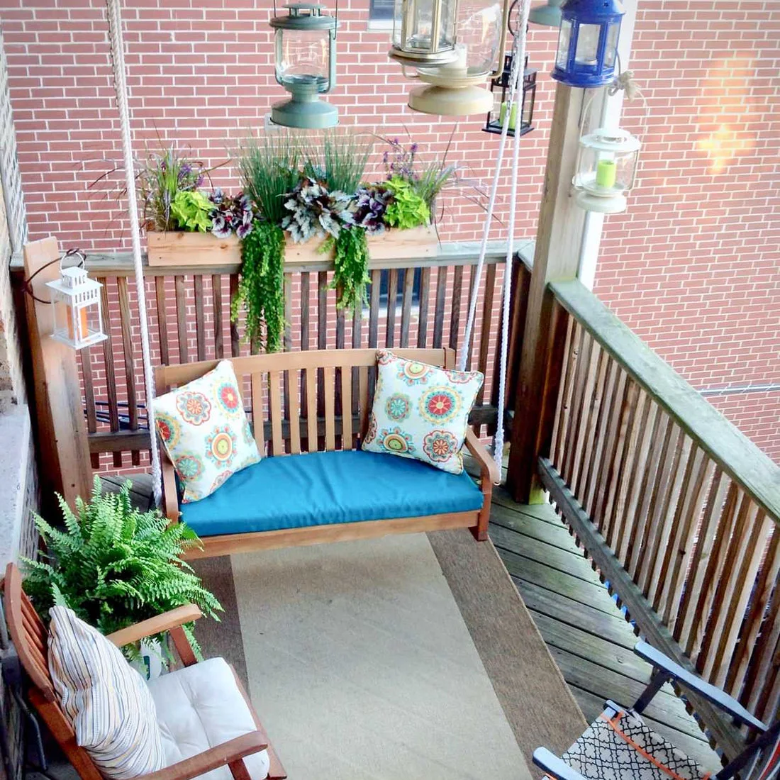 A wooden swing with a blue cushion hangs at the end of a narrow balcony beside planters