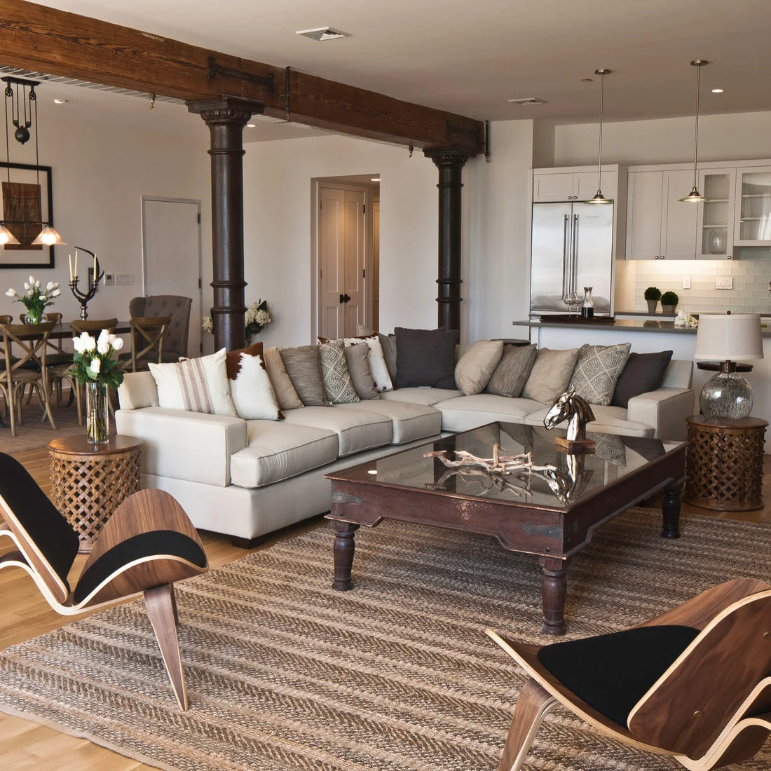 A pale sectional and curved wood chairs beside dark columns and exposed timber beams