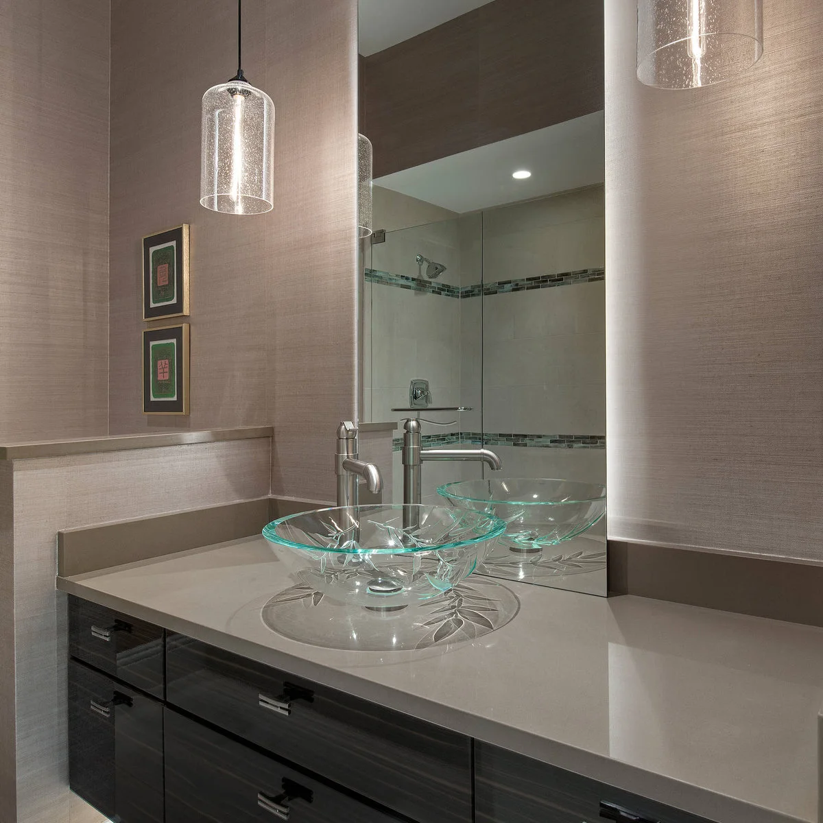 A clear patterned glass vessel bowl sits on a pale counter below a tall mirror, with a tall metal faucet and glass pendant.