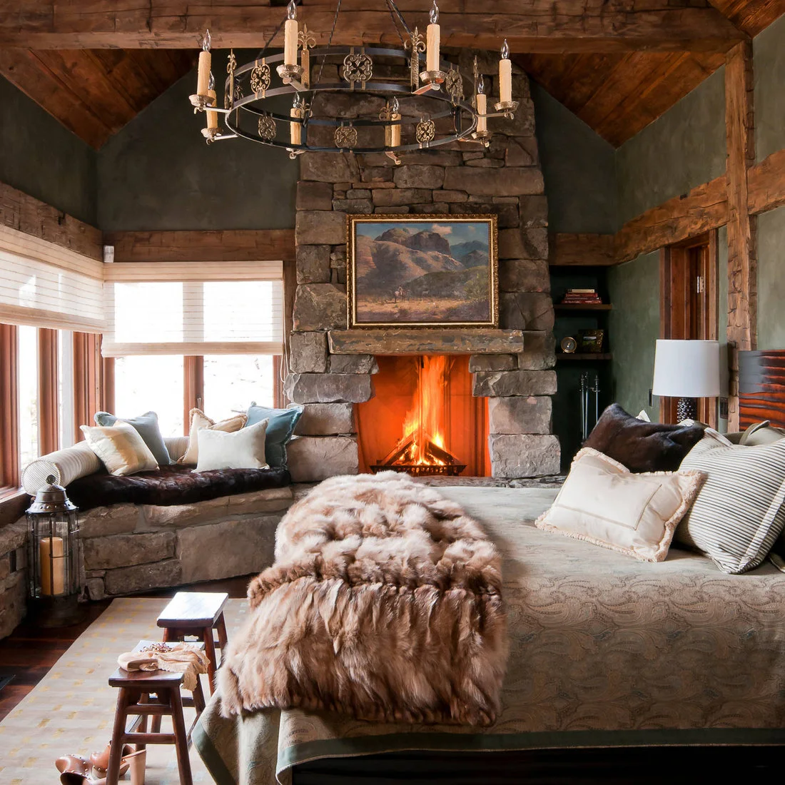 Rustic bedroom with a stone fireplace, framed mountain landscape, timber beams and a cushioned window seat
