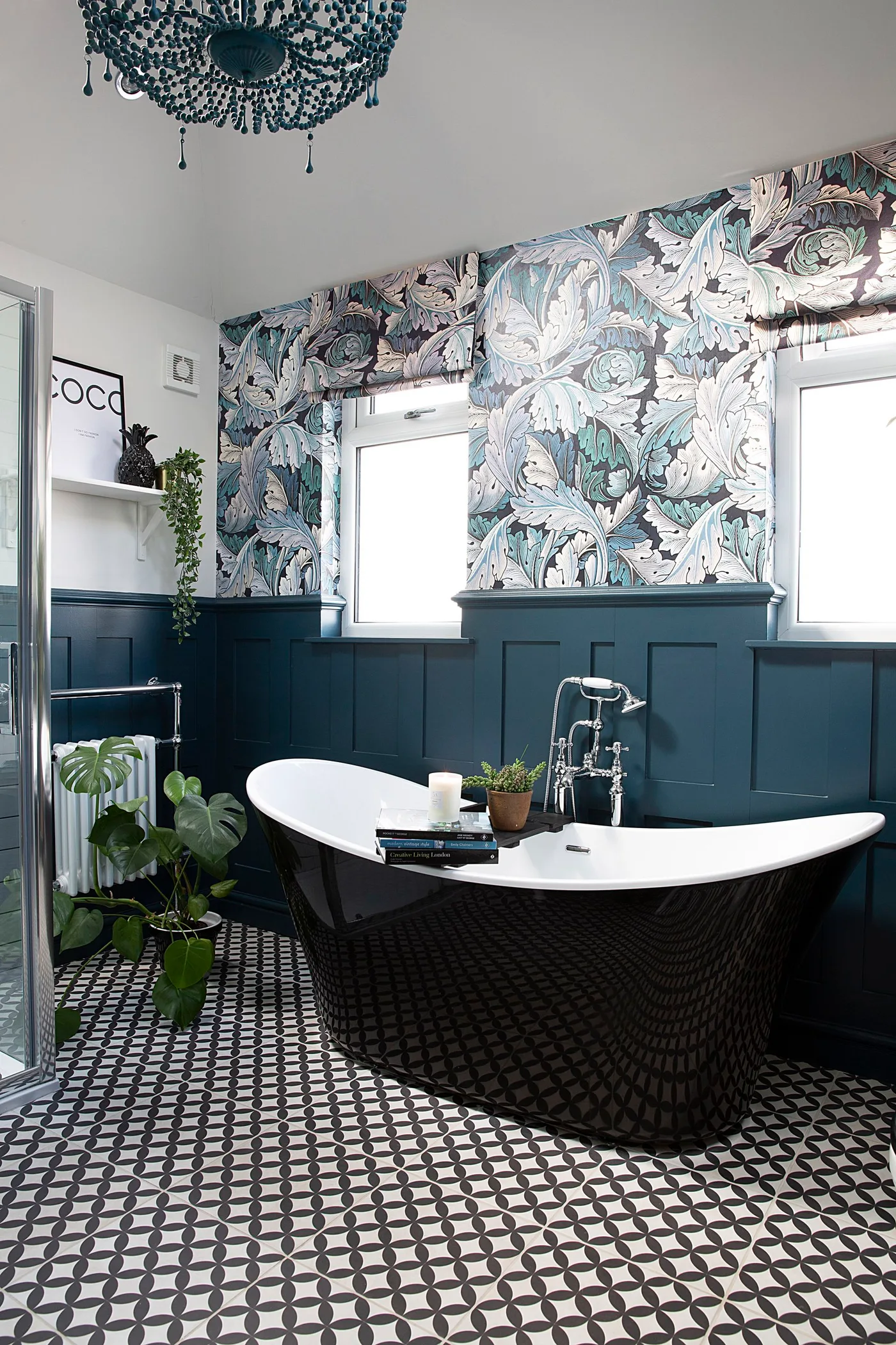 Dark blue lower paneling surrounds a black freestanding bath below floral wallpaper and white window trim