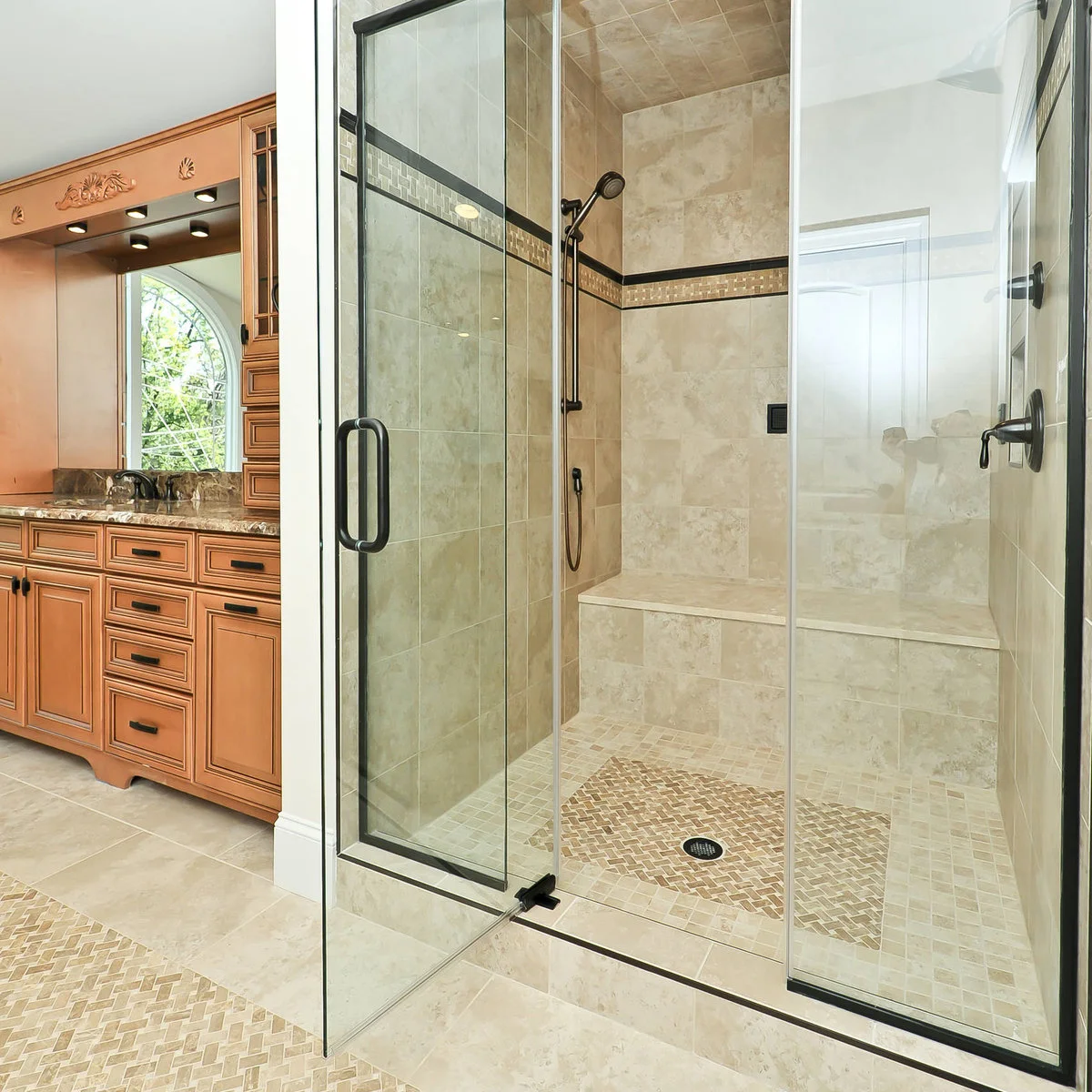 Glass shower with dark hardware and a full-width pale tiled bench