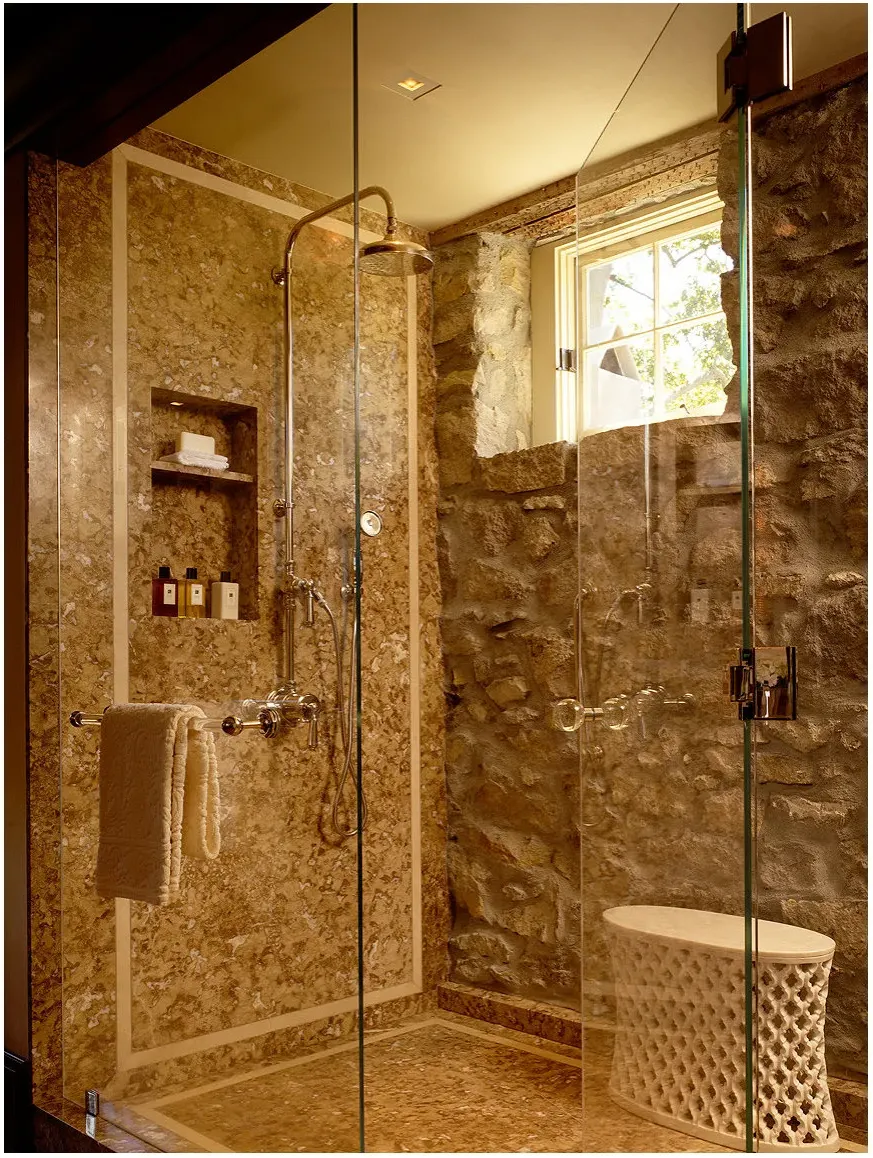 A glass shower with warm patterned wall panels, a rough stone-textured window wall, a tall niche and a small pale stool.