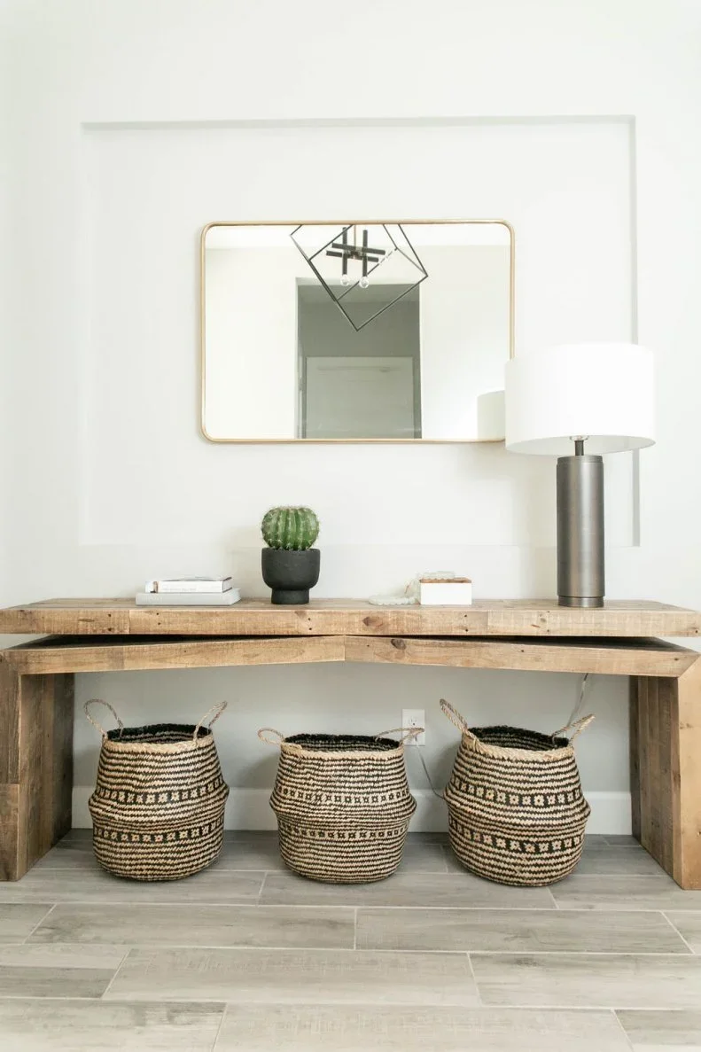 A rough timber console with three woven baskets below a large rectangular mirror