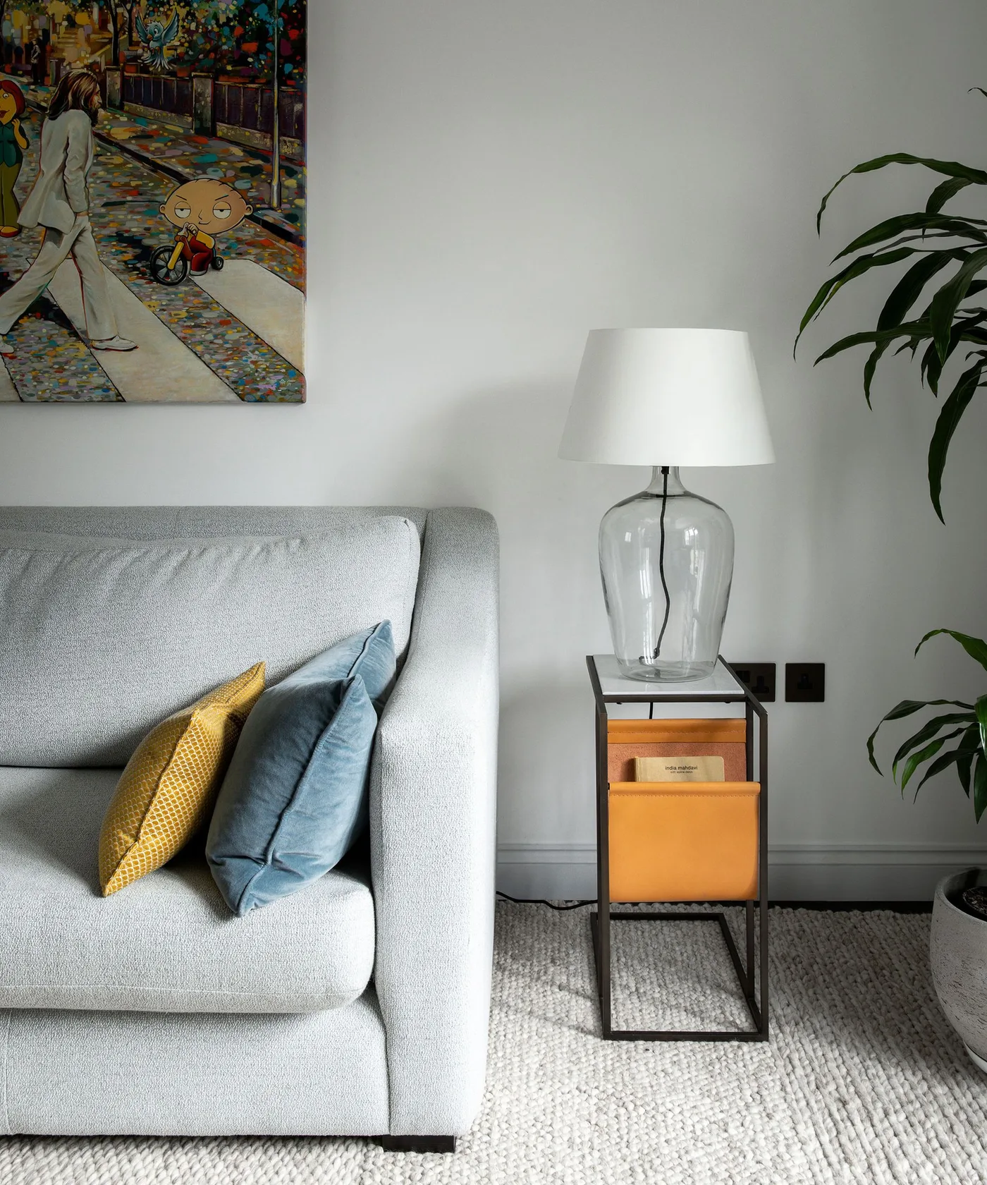 Pale gray sofa with ochre cushion beside a narrow dark lamp stand with warm-colored storage pockets