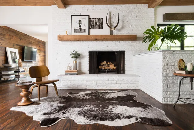 A timber chair and small table sit beside a pale brick fireplace and warm ceiling details.