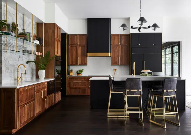 A tall black cabinet stands beside warm timber cupboards and a pale island.
