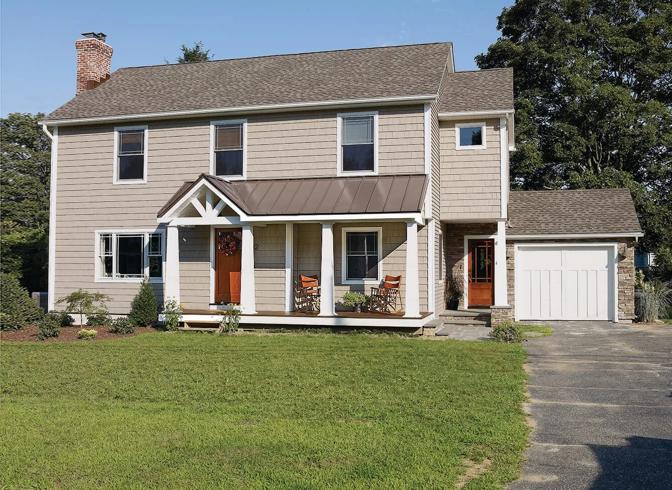 A renovated two-story house with pale shingle siding has a low front porch roof, white posts and two wooden rocking chairs.