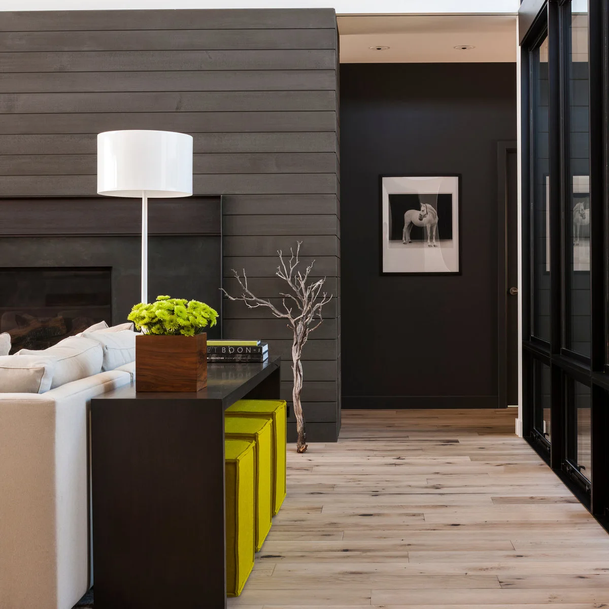 Pale sofa beside dark paneled surfaces with a slim console and bright stools below