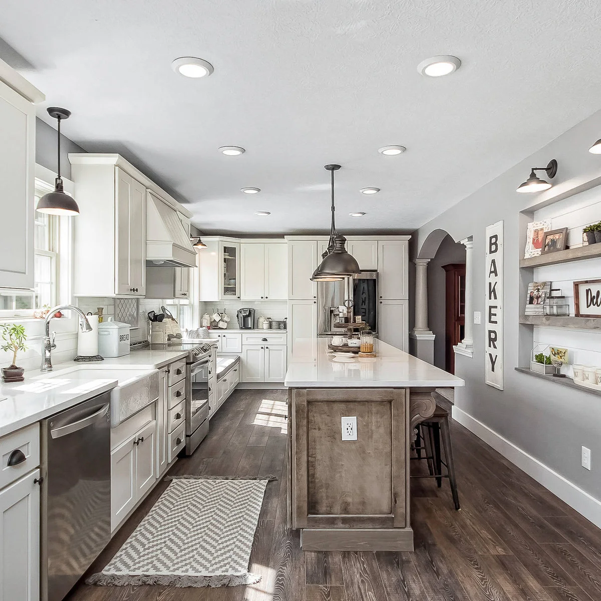 Round low-profile ceiling fittings run through a narrow white kitchen with dark pendants and a wood-toned island.