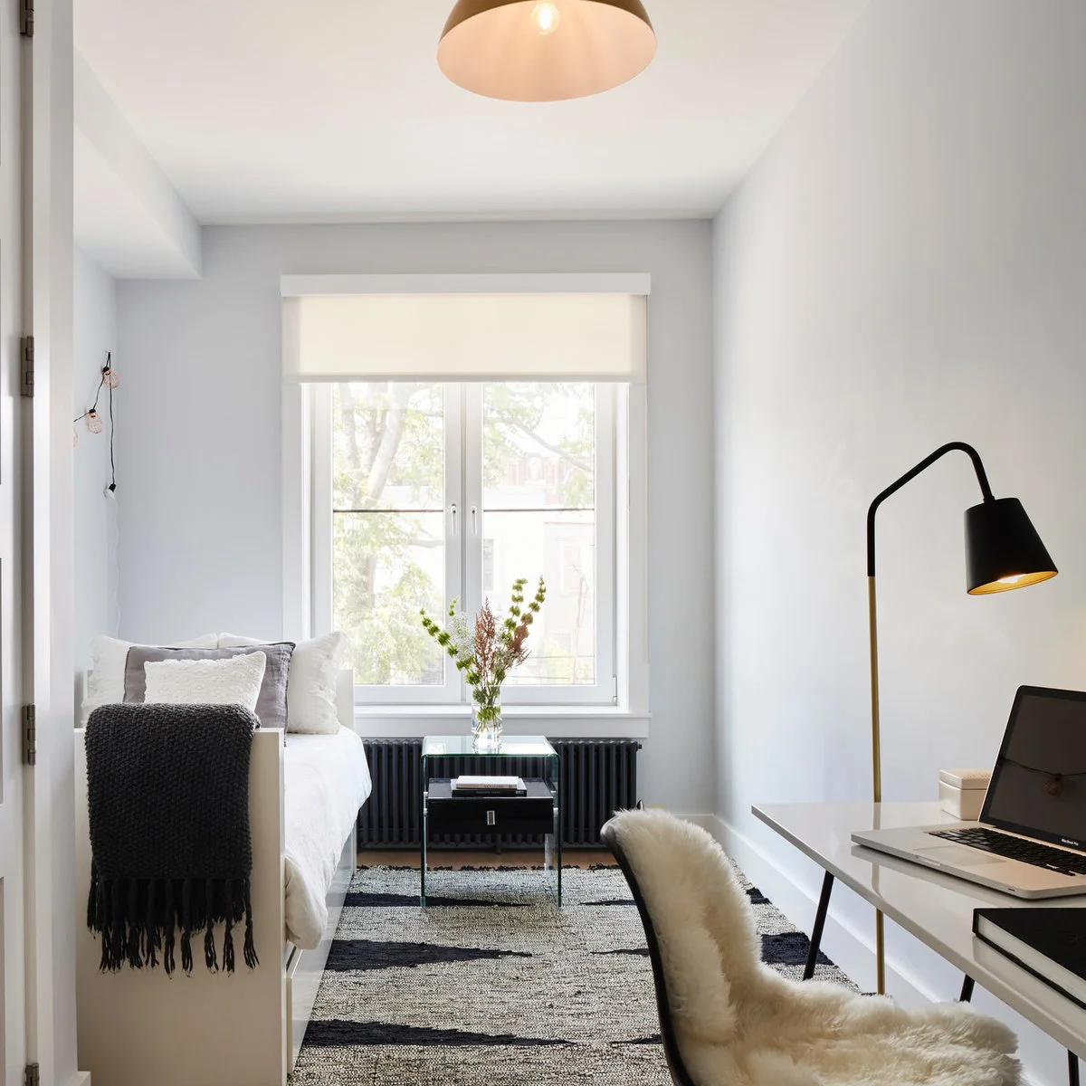 A white daybed runs along one wall of a narrow office opposite a white desk and black task lamp.