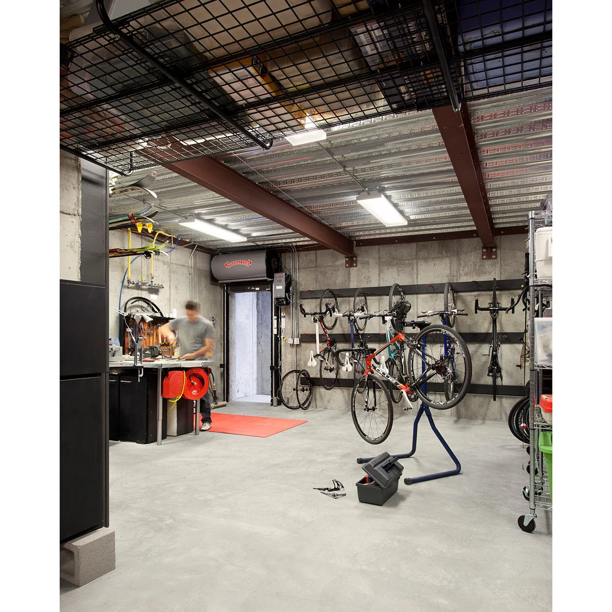 Garage bicycle workshop with wall-hung bikes, a repair stand and a small bench near the entrance.