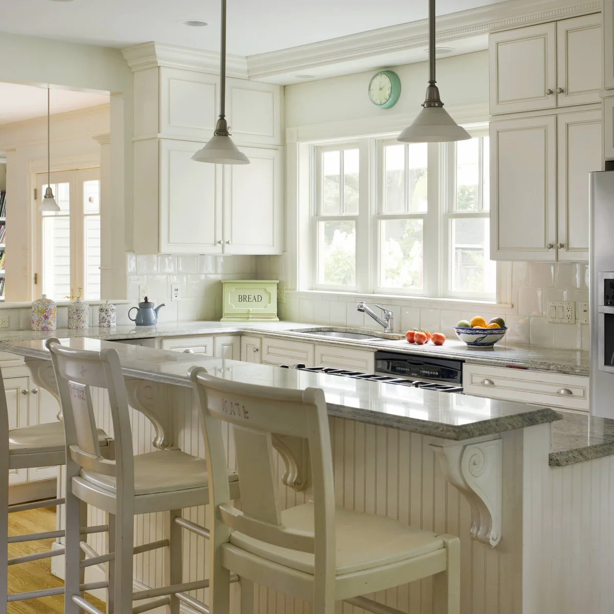 A raised pale breakfast bar with decorative brackets and white stools fronts a cream kitchen.