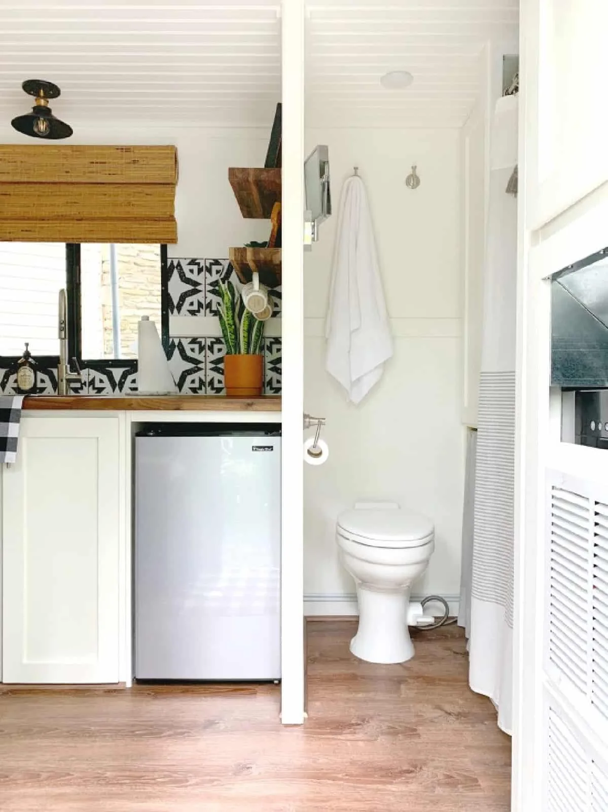 Small white camper toilet compartment with two wall hooks and a towel beside the kitchen refrigerator.