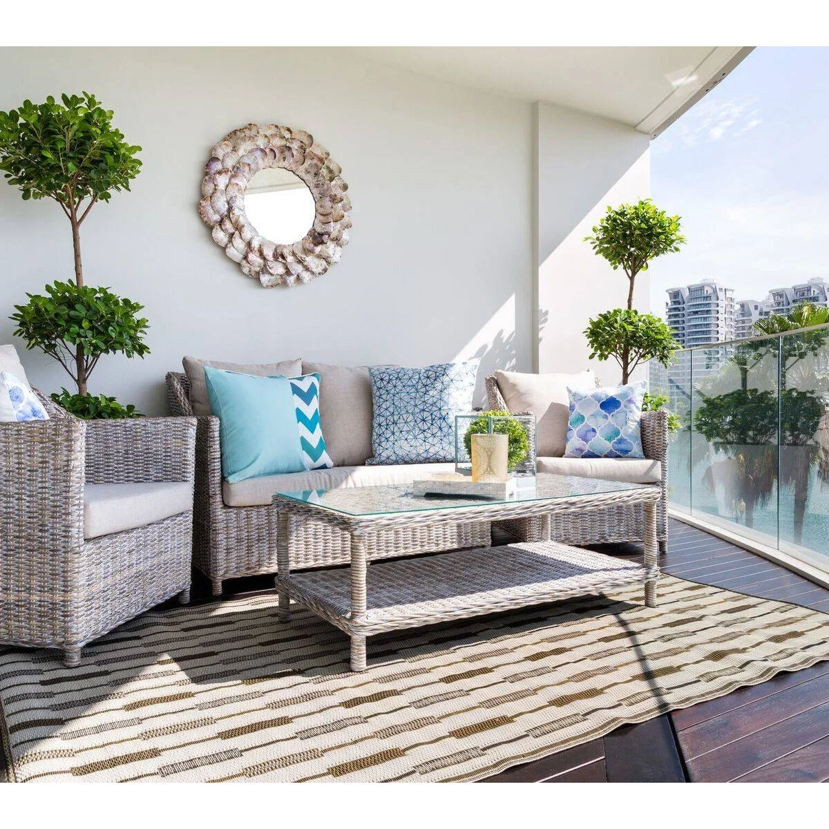 Sheltered balcony with pale woven-looking sofa and chairs, blue cushions and a glass railing