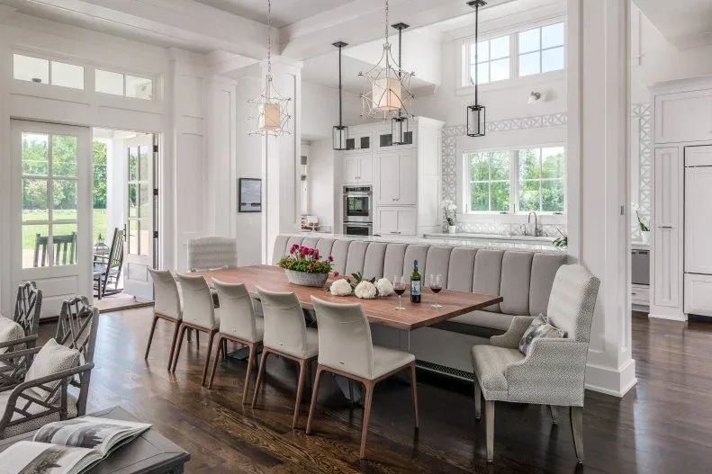 Long wooden dining table with pale chairs, a gray corner banquette and open lantern lights.