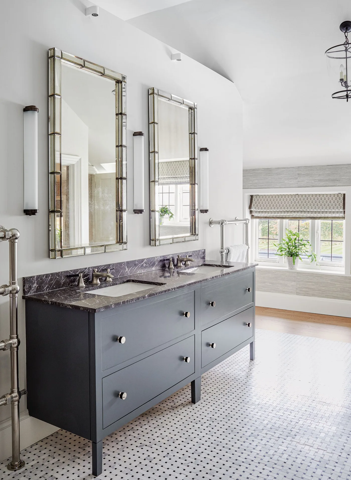 Bright bathroom with a dark gray double vanity on legs, veined countertop, two tall framed mirrors, vertical lights, and dotted floor.
