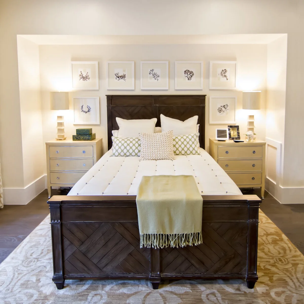 A cream rug with large pale scroll patterns extends in front of a dark wood bed beneath botanical pictures.