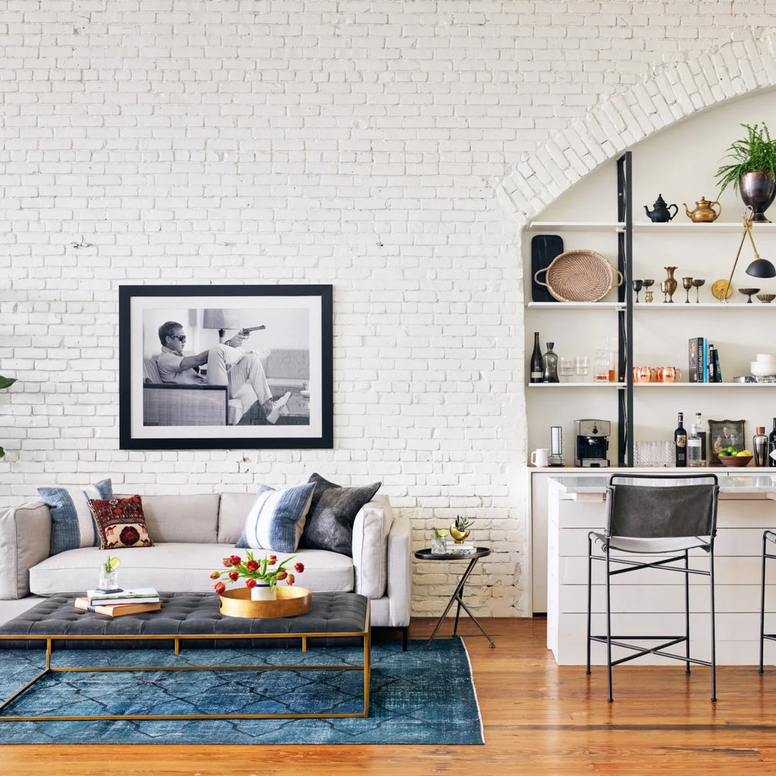 A pale sofa and dark upholstered bench beside white brick, an arched recess and bar shelving