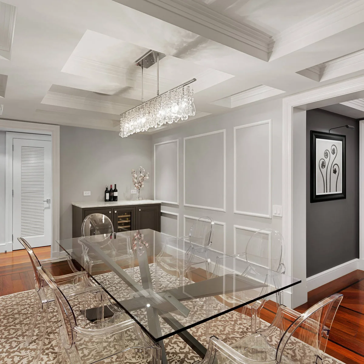 Thin white rectangular wall frames behind a glass dining table and clear chairs