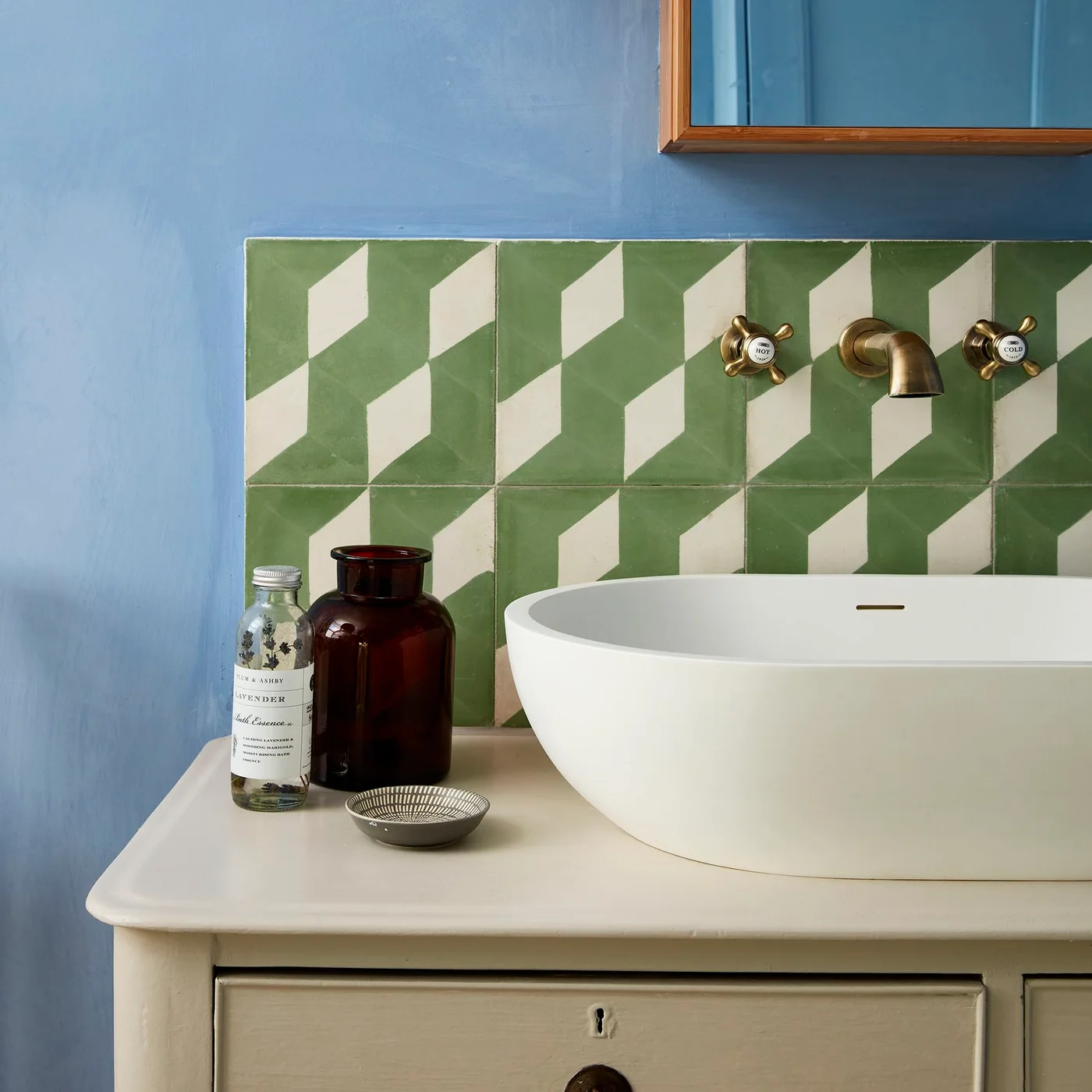 Green and white geometric backsplash behind a white vessel basin against a blue painted wall.
