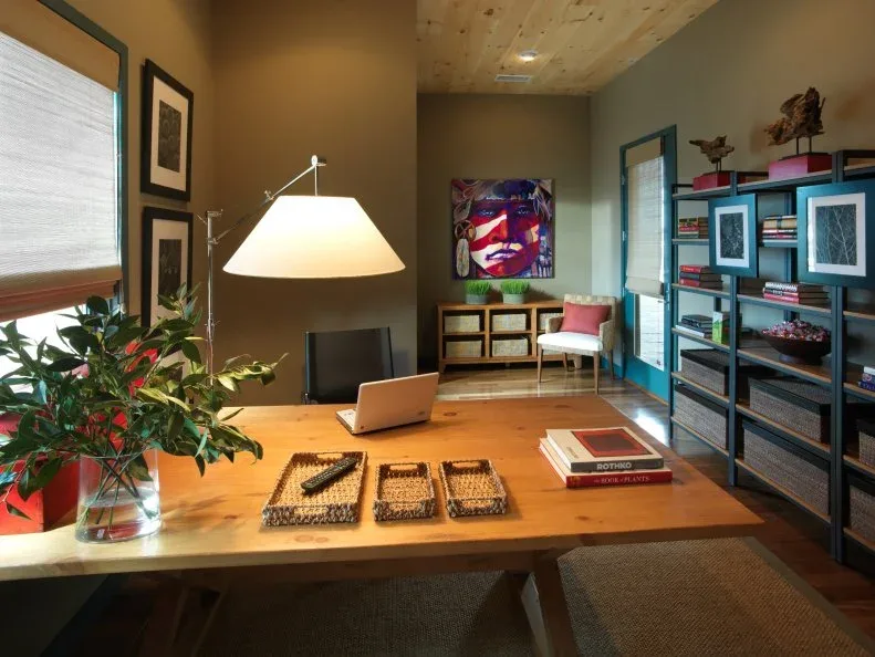 Country-inspired office with wood trestle desk, dark open shelving, basket storage, colorful portrait and blue-trimmed door