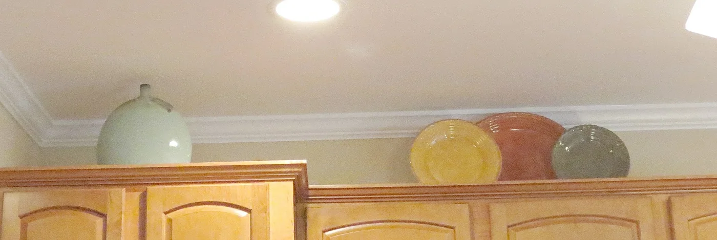 A pale green bottle-shaped vase and three upright plates in yellow, terracotta and gray above warm wood kitchen cabinets.